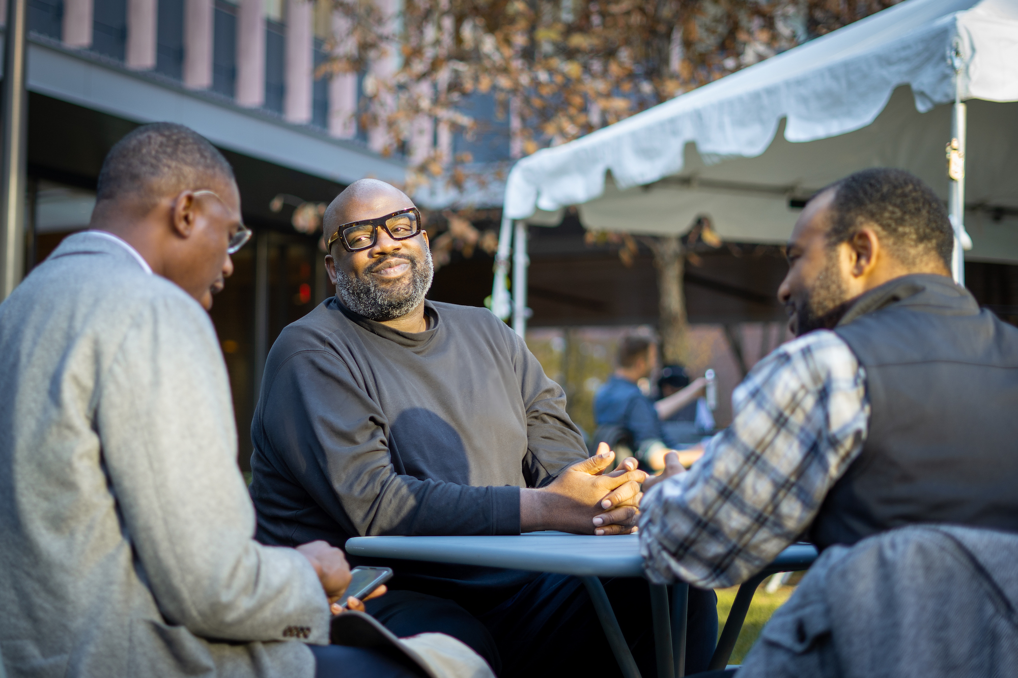 George Greenidge, seated at a table, outside, talking with students Darold Cuba (right) MC/MPA ‘21 and community member like Kalu K. Ugwuomo, Jr. (left) Co-founder and Managing Partner at Kalgomex Ventures