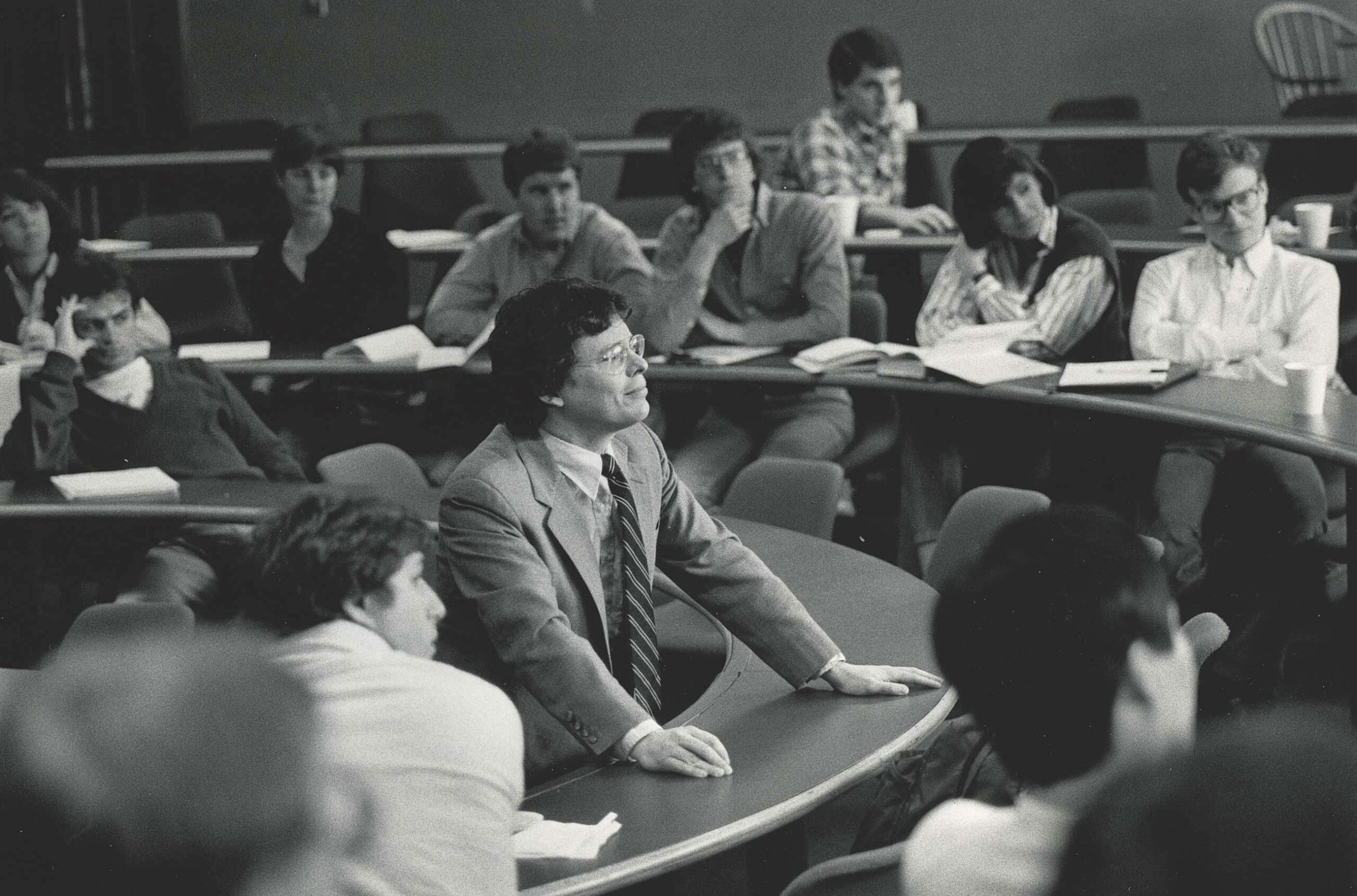 Mark Moore, smiling, stands in the middle of a classroom with students sitting around him on all sides