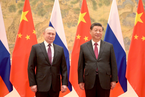 Vladimir Putin stands next to Xi Jinping, both stand in front of a row of Chinese and Russian flags