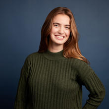 Gina stands in front of a dark blue background wearing a dark green sweater