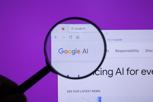 Photo of GoogleAI with a magnifying glass held to the GoogleAI logo