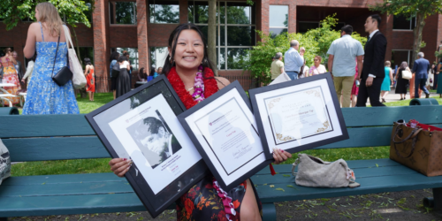 Photo of Caren Yap sitting on a bench at HKS graduation holding three frames