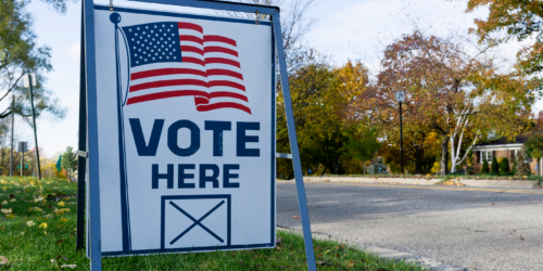 A 'Vote Here' sign on the side of a road.
