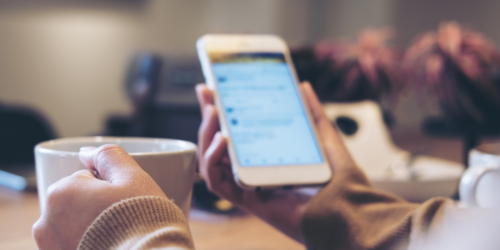 Woman holding phone with a cup of coffee